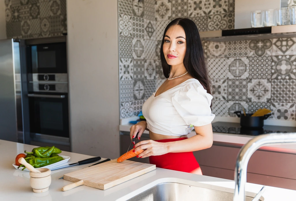 Felicia 'Felix' Hayes looks at the camera with a smile while chopping a fresh carrot on a wooden board in her kitchen.