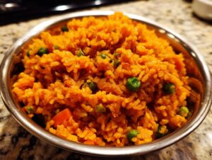 Close-up of bright orange spanish rice mixed with green peas served in a stainless steel bowl.
