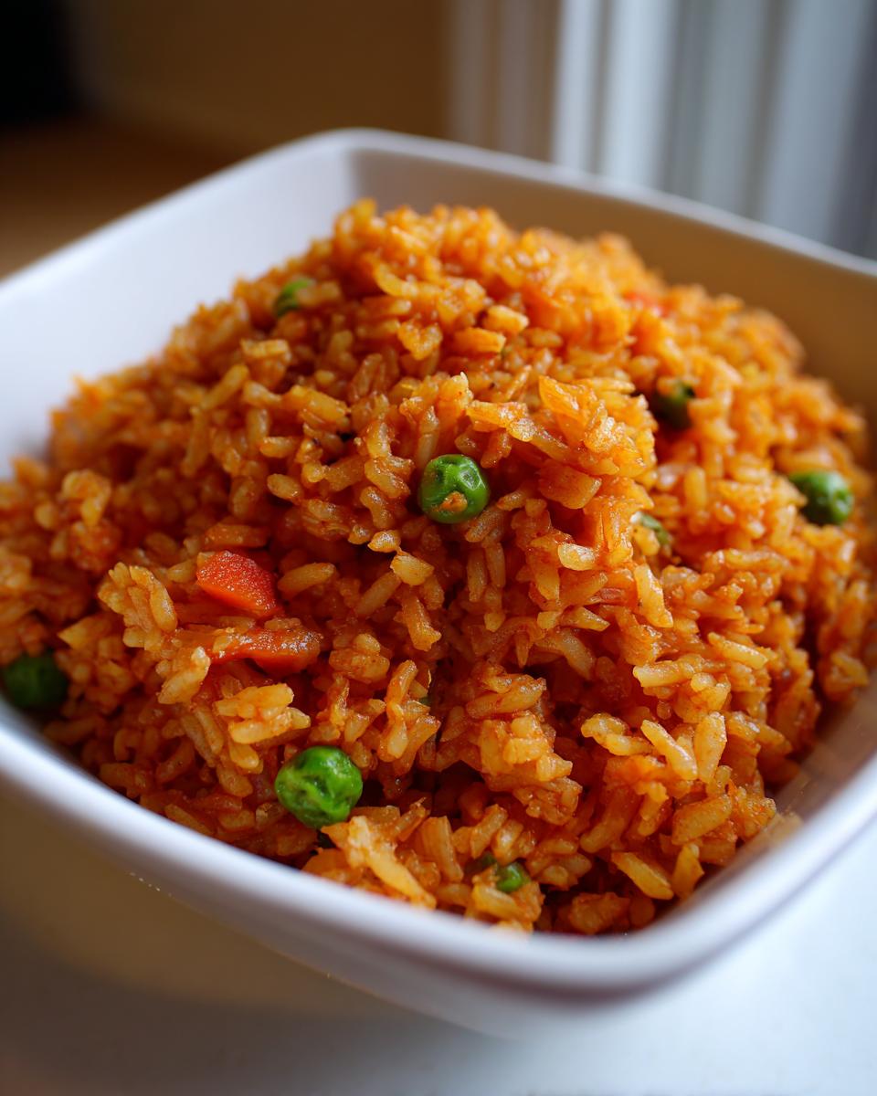 A close-up, high-angle shot of vibrant orange spanish rice mixed with green peas and diced carrots in a white bowl.