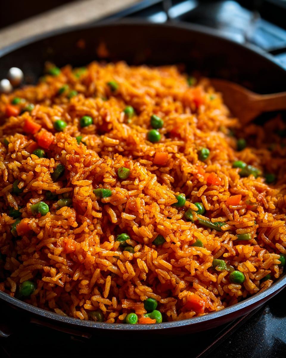 A close-up view of vibrant, orange-red spanish rice cooked in a dark pan, mixed with bright green peas and diced carrots.