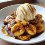 Close-up of caramelized bananas in rich sauce topped with vanilla ice cream, showcasing perfect Bananas Foster.