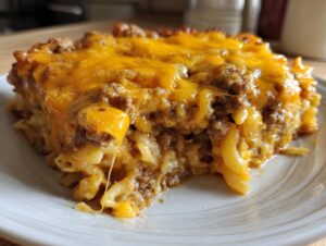 A close-up of a generous serving of cheeseburger casserole featuring ground beef, macaroni, and a thick layer of melted cheddar cheese.