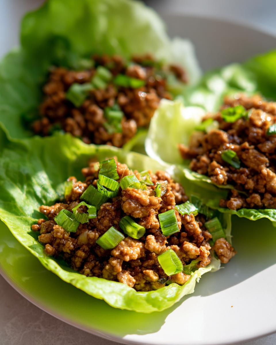 Three servings of savory chicken lettuce wraps topped with fresh green onions on a light plate.