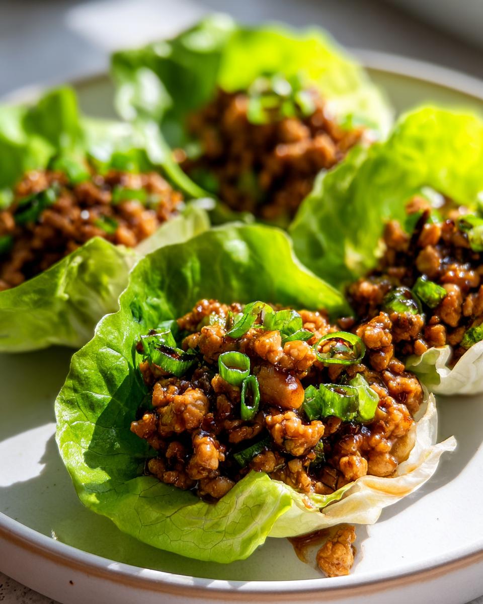 Close-up of several fresh chicken lettuce wraps filled with savory ground chicken mixture and topped with green onions.