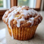 A close-up photo of a freshly baked cinnamon roll muffin topped with thick white icing glaze.