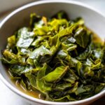 Close-up of a white bowl filled with bright green, tender cooked collard greens simmering in pot liquor.