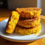 A stack of four golden, crispy fried cornbread patties drizzled with honey on a white plate.