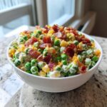 A creamy, vibrant pea salad topped generously with crispy bacon bits and cheese crumbles.