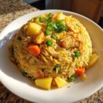 A mound of vibrant pineapple fried rice featuring chunks of pineapple, chicken, peas, and carrots, garnished with green onions.