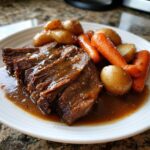 Slices of tender pot roast covered in rich brown gravy, served with roasted carrots and small potatoes.