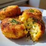 Close-up of golden brown, crispy potato croquettes, one broken open showing a cheesy, fluffy interior topped with fresh chives.