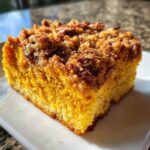 Close-up of a moist slice of pumpkin crunch cake showing the bright orange cake layer and crunchy brown pecan topping.