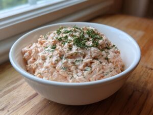 A generous serving of creamy pink smoked salmon dip topped with fresh dill in a white bowl.