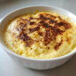 Close-up of a creamy, baked egg custard in a white ramekin with a lightly browned, spiced top.