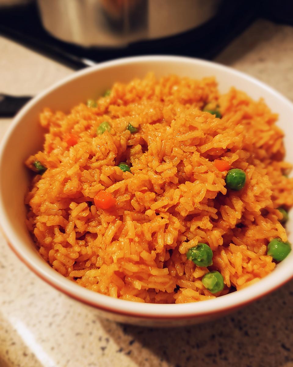 Close-up of a white bowl filled with vibrant orange spanish rice mixed with bright green peas and small pieces of carrot.