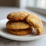 A stack of three chewy brown butter sugar cookies rolled in sparkling sugar, with one cookie broken to show the soft interior.