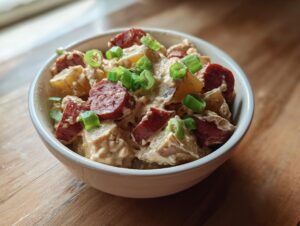 A close-up of a bowl filled with creamy Cajun potato soup chunks, sliced sausage, and green onions.