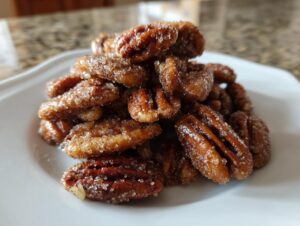 A pile of freshly made candied pecans recipe nuts coated in sparkling sugar and cinnamon on a white plate.