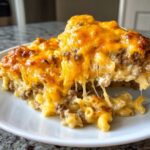 A serving of rich cheeseburger casserole lifted from a plate, showing ground beef, macaroni, and a dramatic, gooey cheese pull.