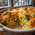 Close-up of a creamy, cheesy broccoli casserole with a golden crust, served hot in a white baking dish.