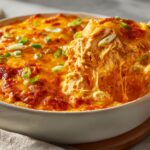 A spoonful of hot, cheesy Buffalo chicken dip showing stringy cheese pull and shredded chicken.