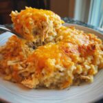 A spoonful of creamy cheesy chicken and rice being lifted, showing long cheese pulls from the baked topping.
