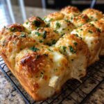 Close-up of cheesy hawaiian roll garlic bread topped with melted cheese and fresh parsley on a cooling rack.