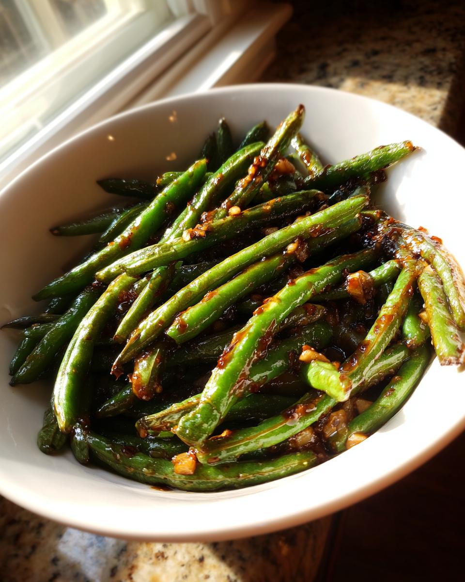 A white bowl filled with glossy, bright green chinese green beans with garlic sauce.