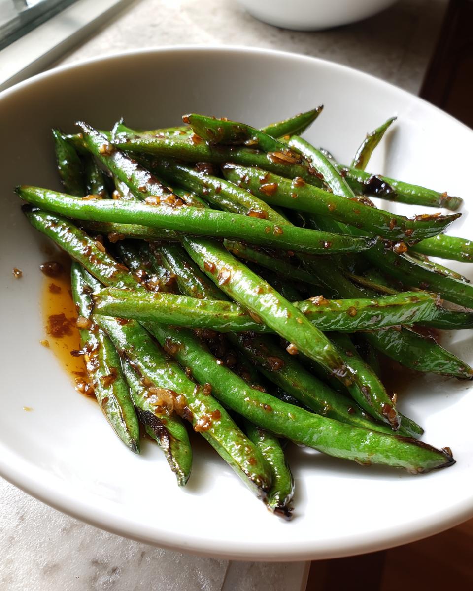 A close-up of vibrant green beans tossed in a savory brown garlic sauce, ready to serve.