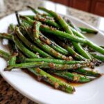 Bright green, stir-fried chinese green beans with garlic sauce glistening on a white plate.