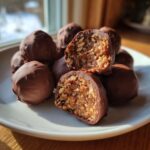 A pile of chocolate-covered pecan pie balls, with one cut in half showing the rich, chunky pecan filling inside.