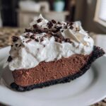 A decadent slice of Christmas chocolate cream pie featuring a dark crust, rich chocolate filling, and generous whipped cream topped with chocolate shavings.