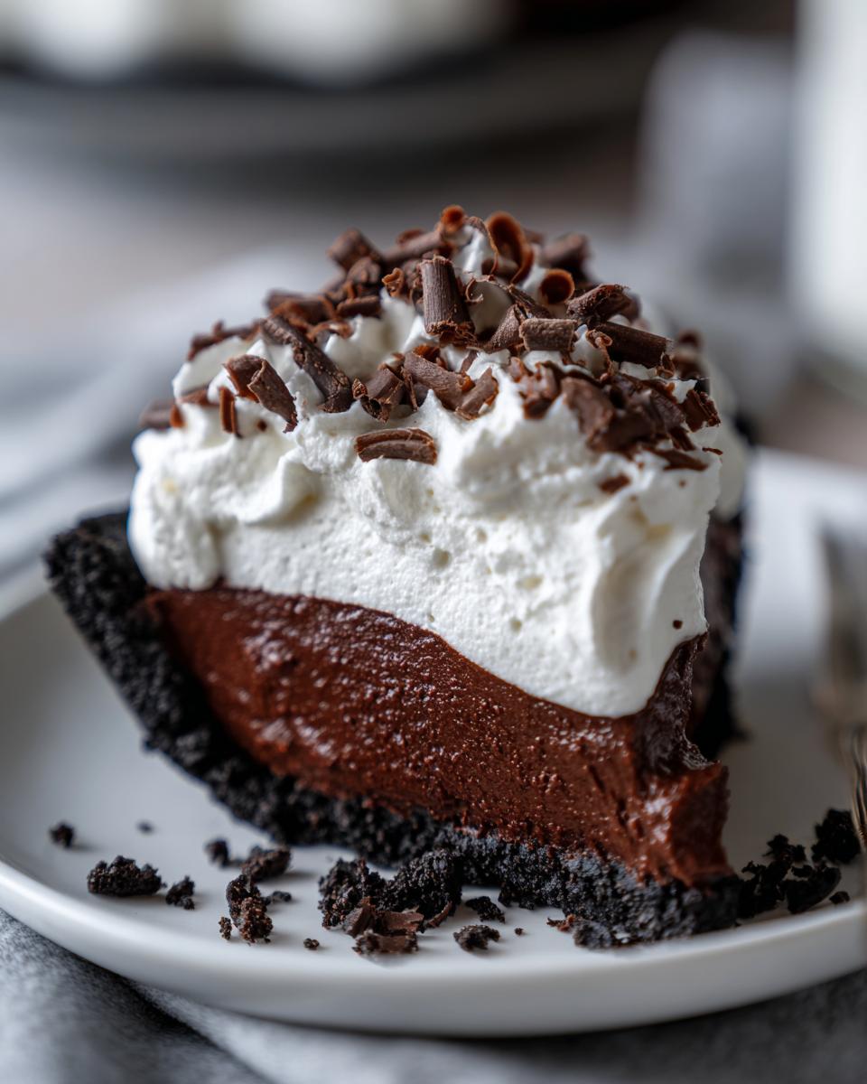Close-up of a slice of Christmas chocolate cream pie featuring a dark crust, rich filling, and whipped cream topped with chocolate shavings.