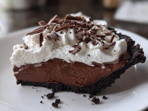 A rich slice of Christmas chocolate cream pie featuring a dark crust, thick chocolate filling, and whipped cream topped with chocolate shavings.