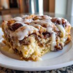 A close-up of a moist slice of Cinnamon Roll Casserole topped generously with white vanilla icing.