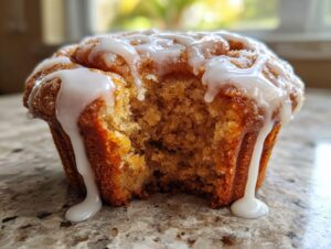 Close-up of a single, glazed cinnamon roll muffin with a bite removed, showing the soft interior.