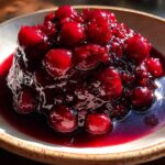 A close-up, appetizing shot of thick, glossy cherry pie filling with whole, bright red cherries.
