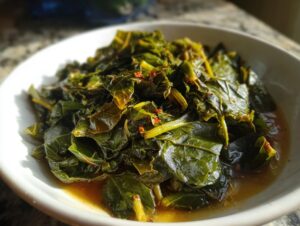 Close-up of tender, dark green collard greens served in a white bowl with savory broth and red pepper flakes.