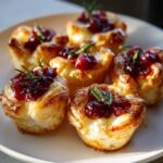 Close-up of golden baked cranberry brie bites made with flaky pastry, topped with cranberry sauce and rosemary.