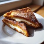 Two golden-brown halves of cream cheese stuffed french toast dusted with powdered sugar on a white plate.