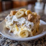 A generous slice of creamy banana pudding topped with whipped cream, fresh banana slices, and vanilla wafers.