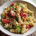 Close-up of a bowl of creamy blt pasta salad featuring fusilli pasta, cherry tomatoes, bacon bits, and lettuce.