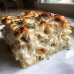 A close-up shot of a serving of rich Chicken Alfredo Lasagna showing layers of pasta, white sauce, and shredded chicken.