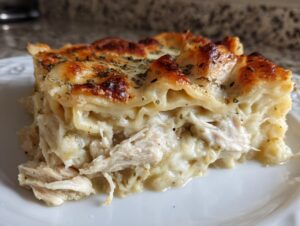Close-up of a rich slice of chicken alfredo lasagna showing layers, shredded chicken, and a browned, cheesy top.