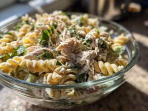 Close-up of a glass bowl filled with creamy chicken caesar pasta salad featuring rotini pasta, shredded chicken, and greens.