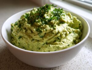 Close-up of a bowl filled with creamy, light green black bean dip, generously garnished with fresh chopped parsley.