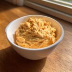 A close-up of creamy, orange pumpkin fluff served in a small white bowl on a wooden surface.
