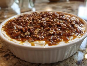 A white, fluted dish filled with creamy pecan pie dip, generously topped with glazed pecans.