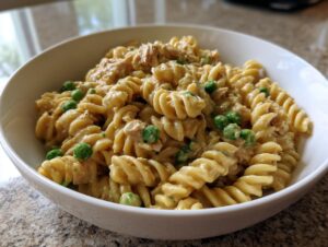 A close-up of creamy tuna pasta made with fusilli noodles and bright green peas served in a white bowl.