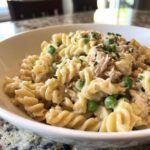 Close-up of creamy tuna pasta made with rotini, peas, and flaked tuna, garnished with parsley.